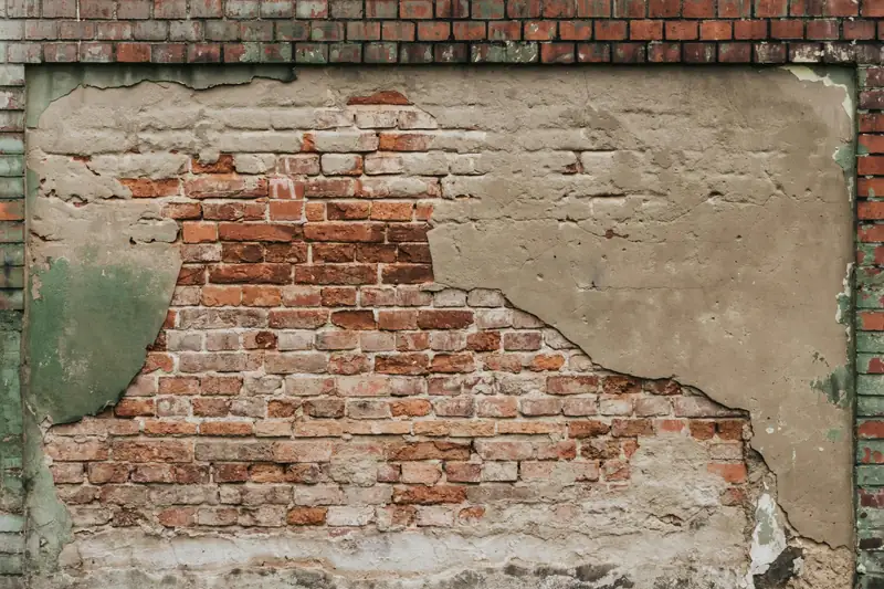 Mur dont l’enduit tombe par plaques et laisse voir la brique ancienne