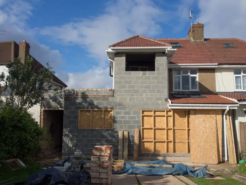 Extension de maison montée en blocs, ouvertures encore fermées de panneaux de bois