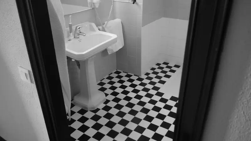 Lavabo sur colonne vu par l’embrasure d’une porte, sol en damier noir et blanc
